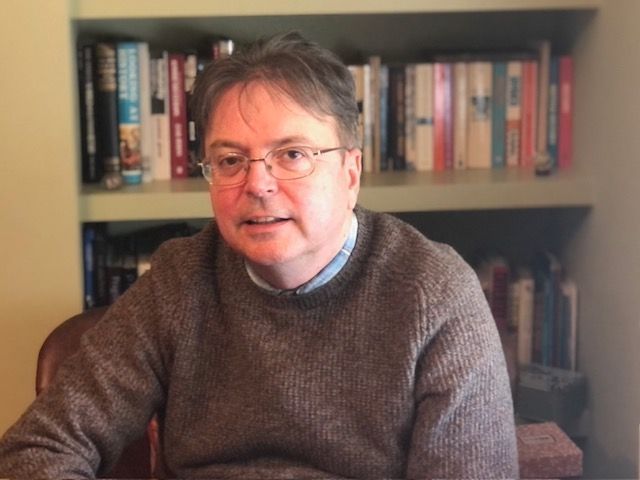 Ceri Jones wears a brown crew neck jumper in his home office